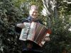 colour photo of Camilla smiling while playing her accordian, in front of a background of trees.