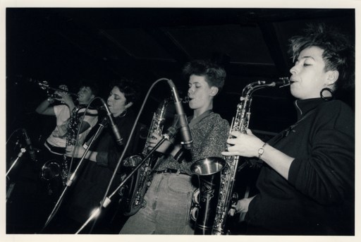 First of four black and white photos of the Deltones first gig, at London's Sol y Sombre club, shows three women saxophone players and a trumpeter blowing strongly into microphones.
