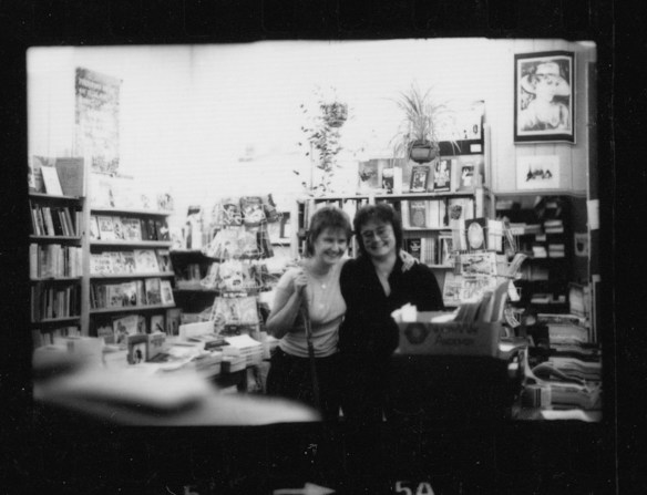 Two women workers at Sisterwrite smiling, lots of bookshelves and posters in background.