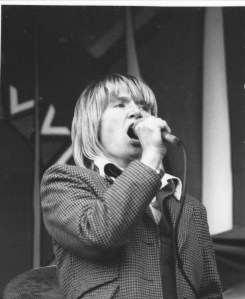 Barbara singing into a hand held mike, at the back of the stage are large Gay Pride banners.