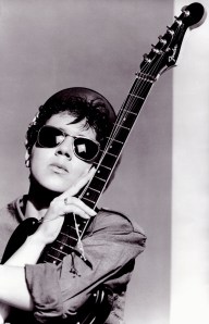 A black and white publicity shot of Georgette, wearing dark glasses and holding an electric guitar, looking serious.