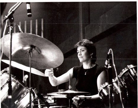 Close up of Jackie Crew behind her drum kit, playing cymbal and snare drum.