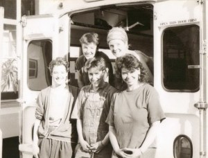 The Fabulous Dirt Sisters stand outside their van, 'nee-naw.' Black and white photo. Smiling. 