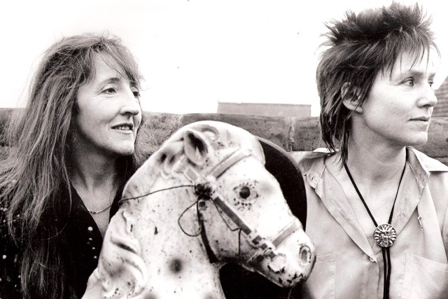 A black and white publicity outdoor shot of Lazy Country. The two women look out of the photo to the right, as does a toy horse's head. Other props are a cowboy-style necktie and hat.