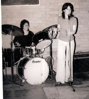 Drummer and vocalist in rehearsal in a university hall, singer playing tambourine.