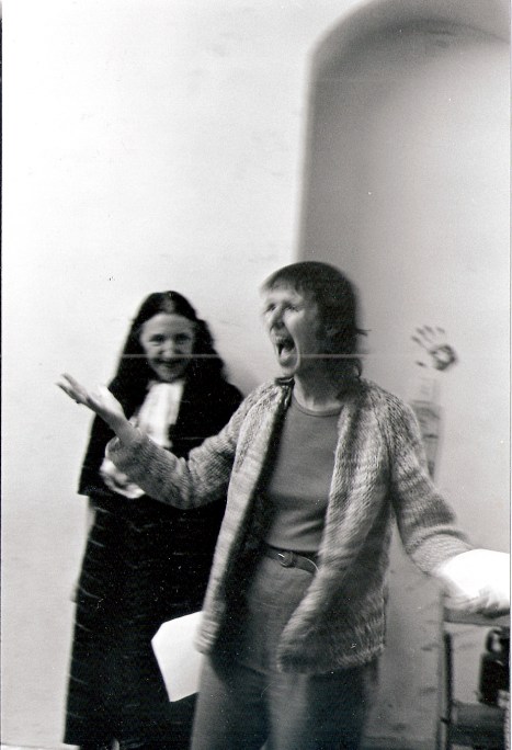 Black and white photograph of Maggie Nicols singing, her arms and mouth open in creative expression, Zouina watching in smiling.