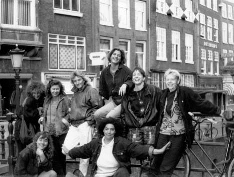 The nine women of Meet Your Feet posing on a bridge in Amsterdam smiling and excited.