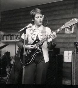 Nony the guitarist in rehearsal, playing and focusing on the guitar's fretboard.