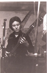 Patsy playing bass guitar at a gig, microphones visible.