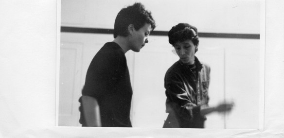 Pauline and Nina dancing, both wearing black, Nina in trademark cap