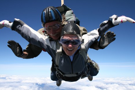 Bright Picture of Peggy skydiving, arms spread against the sky, smiling and floating.