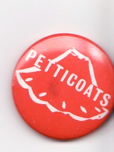 A pink badge with 'Petticoats' written in white letters, over a drawing of the outline of a flared petticoat.