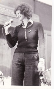 Black and white photo of Ruthie, smiling and singing into a hand held microphone.