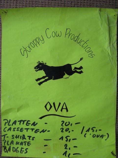 Selling In Germany A poster with green background, black letters, Stroppy Cow Productions logo of a dancing cow, and a list of items of merchandise, t-shirts, badges, cassettes, in German.