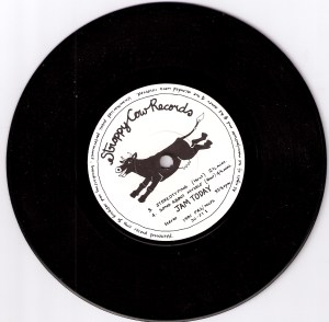 A photo of the E.P. record Stereotyping, with the name Stroppy Cow Records hand written and the label's logo of a cartoon of a happy, dancing cow in black on white background. Track titles Stereotyping and Song About Myself are also printed on the label.