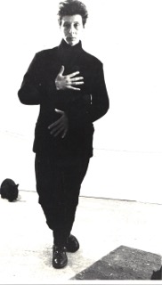 Nina Rapi, dressed in black, against a white background, with a black rabbit behind her.