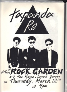 The three band members, dressed in black and white shirts and braces, dark sunglasses, with a large black triangle above them, advertising a gig at the Rock Garden.