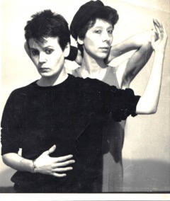 Two women in black and white photo posing with arms bent.