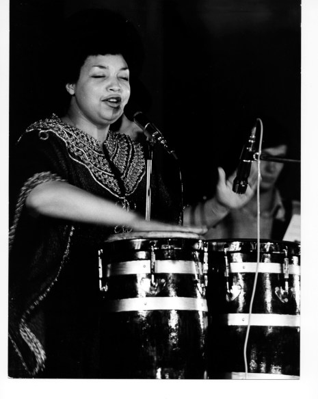 Terri Quaye on stage playing conga drums and singing.