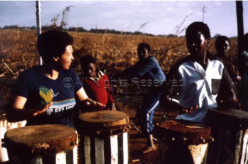 Terri playing conga drums with other musicians, outdoors in Zimbabwe.