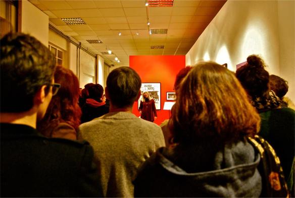 Frankie Armstrong sings at the back of the room, the backs of several heads are included in the shoot, watching her sing.
